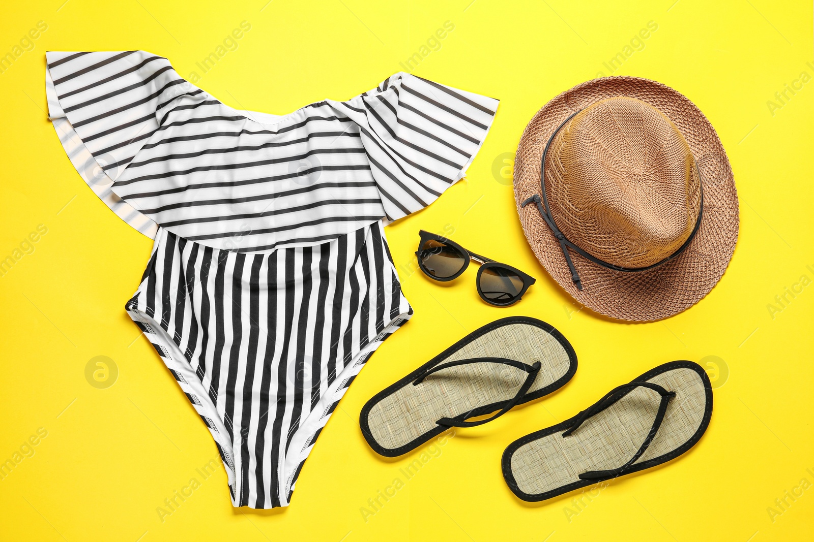 Photo of Flat lay composition with striped swimsuit and beach accessories on yellow background