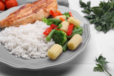Grilled chicken breast and rice served with vegetables on white tiled table, closeup