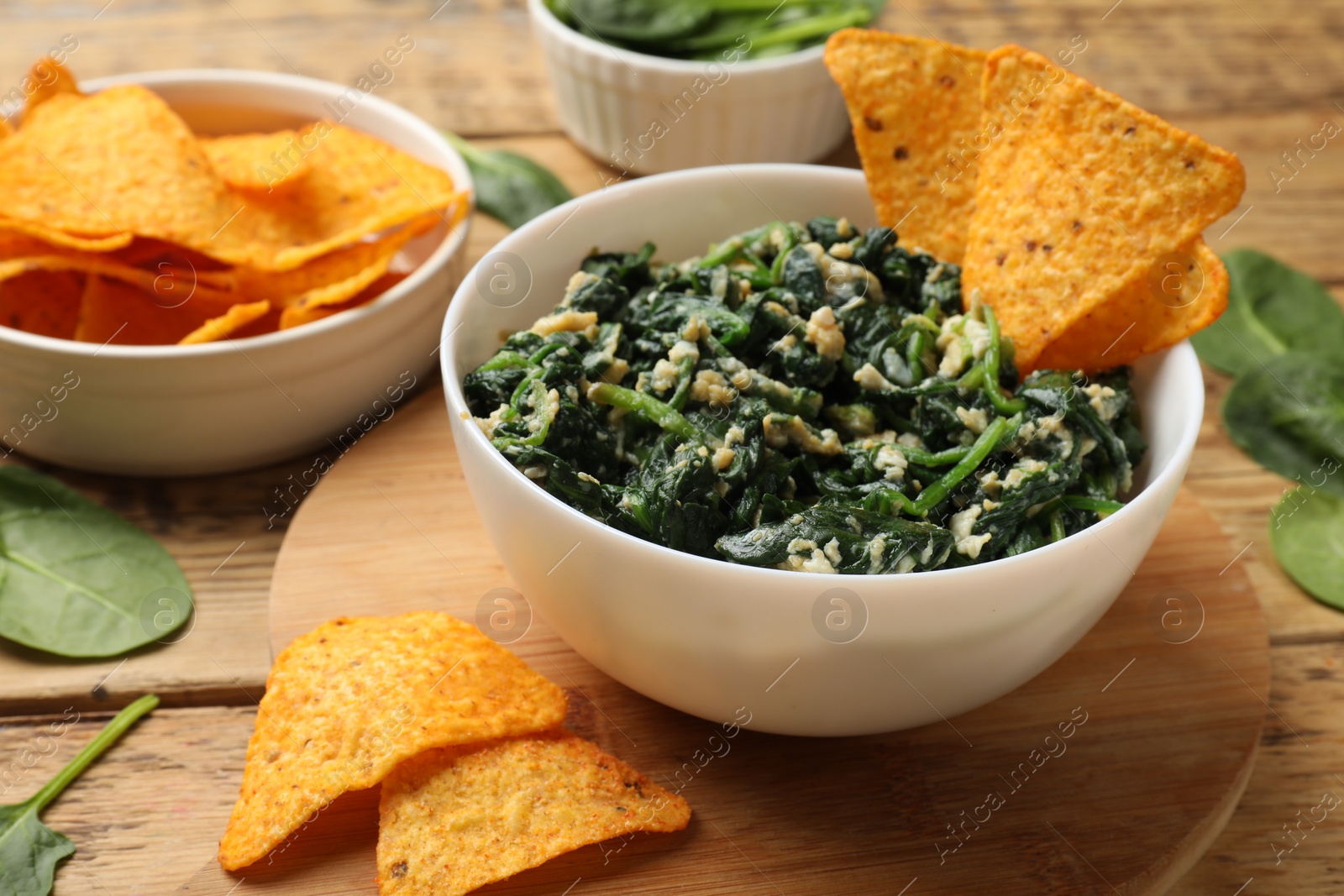 Photo of Tasty spinach dip with eggs in bowl and nachos chips on wooden table, closeup