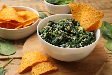 Photo of Tasty spinach dip with eggs in bowl and nachos chips on wooden table, closeup