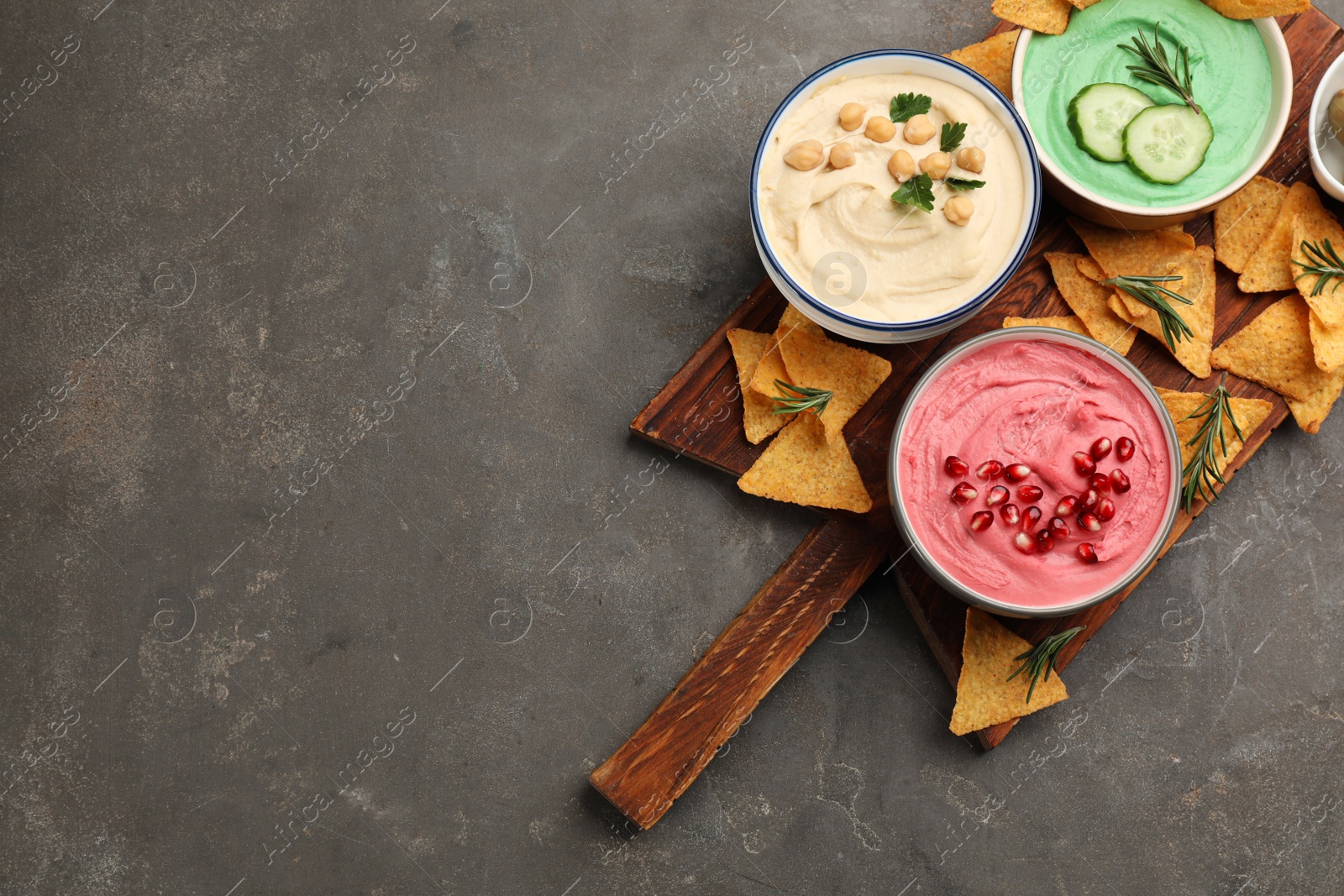 Photo of Different kinds of tasty hummus served with nachos on grey table, top view. Space for text