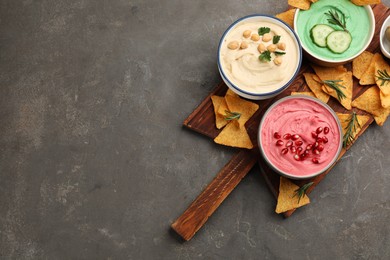 Photo of Different kinds of tasty hummus served with nachos on grey table, top view. Space for text