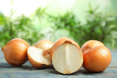 Photo of Ripe onions on blue wooden table against blurred background, space for text