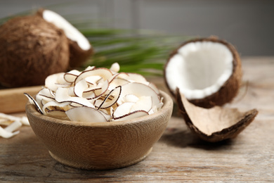 Tasty coconut chips in bowl on wooden table