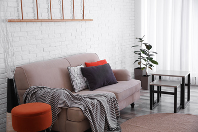 Soft pillows on sofa near white brick wall at home