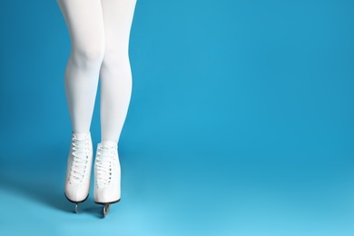 Photo of Woman in elegant white ice skates on light blue background, closeup of legs. Space for text