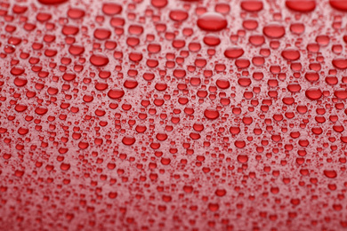 Photo of Water drops on red background, closeup view