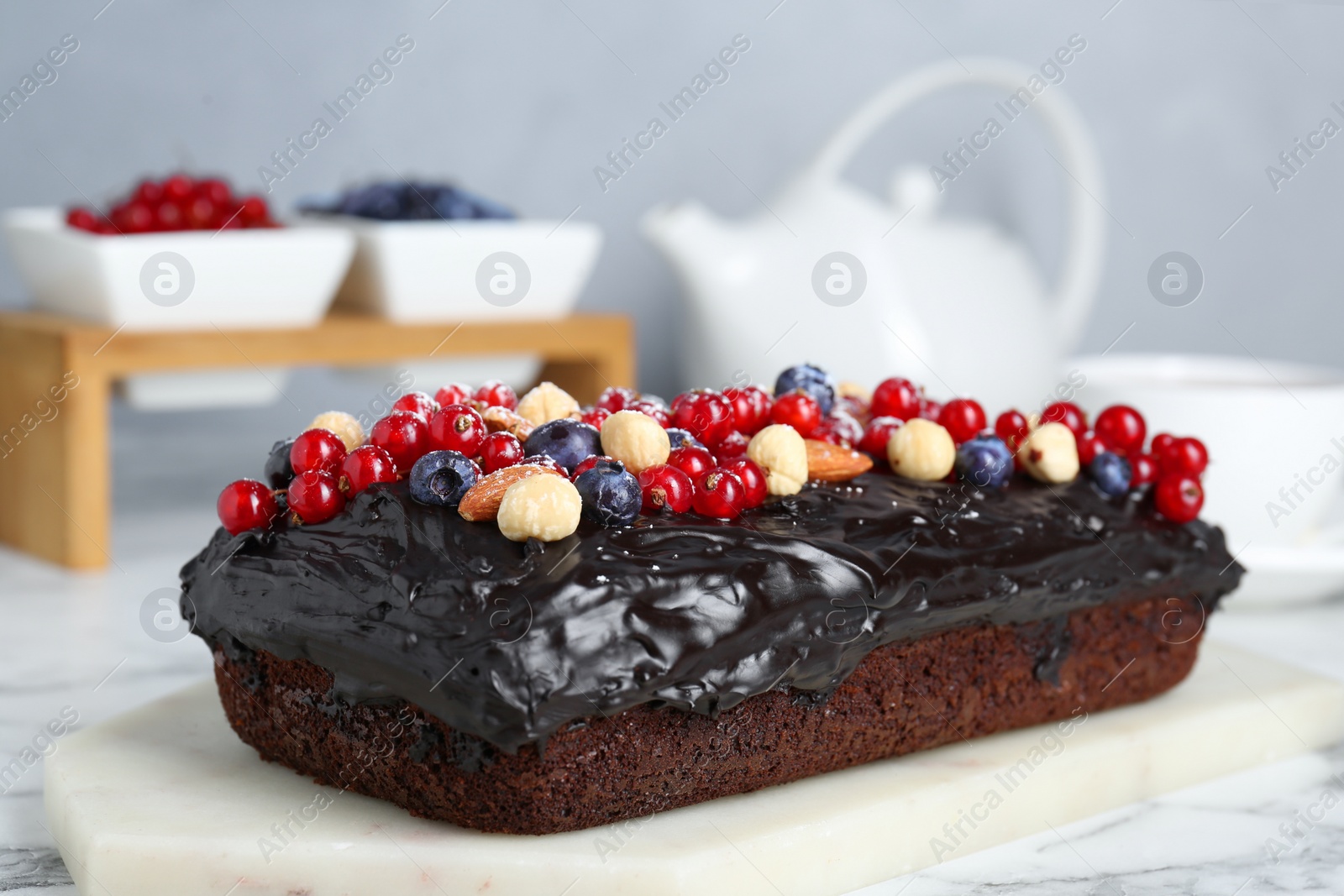 Photo of Delicious chocolate sponge cake with berries and nuts on white marble table, closeup