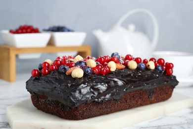 Delicious chocolate sponge cake with berries and nuts on white marble table, closeup