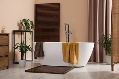 Stylish bathroom interior with ceramic tub, terry towels and houseplants