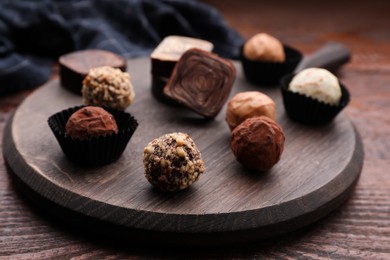 Photo of Different tasty chocolate candies on wooden board, closeup