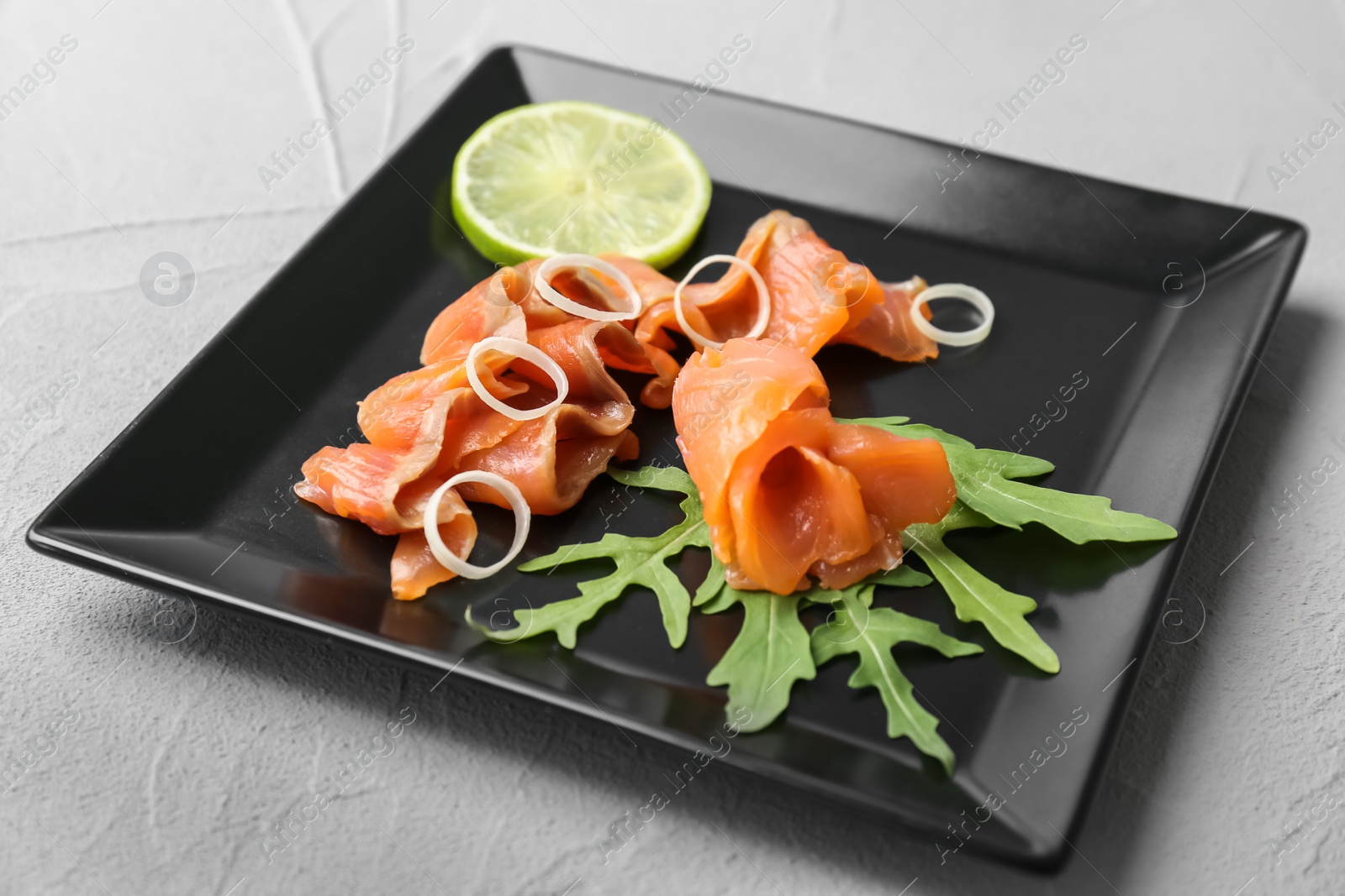 Photo of Plate with fresh sliced salmon fillet, lemon and arugula on table