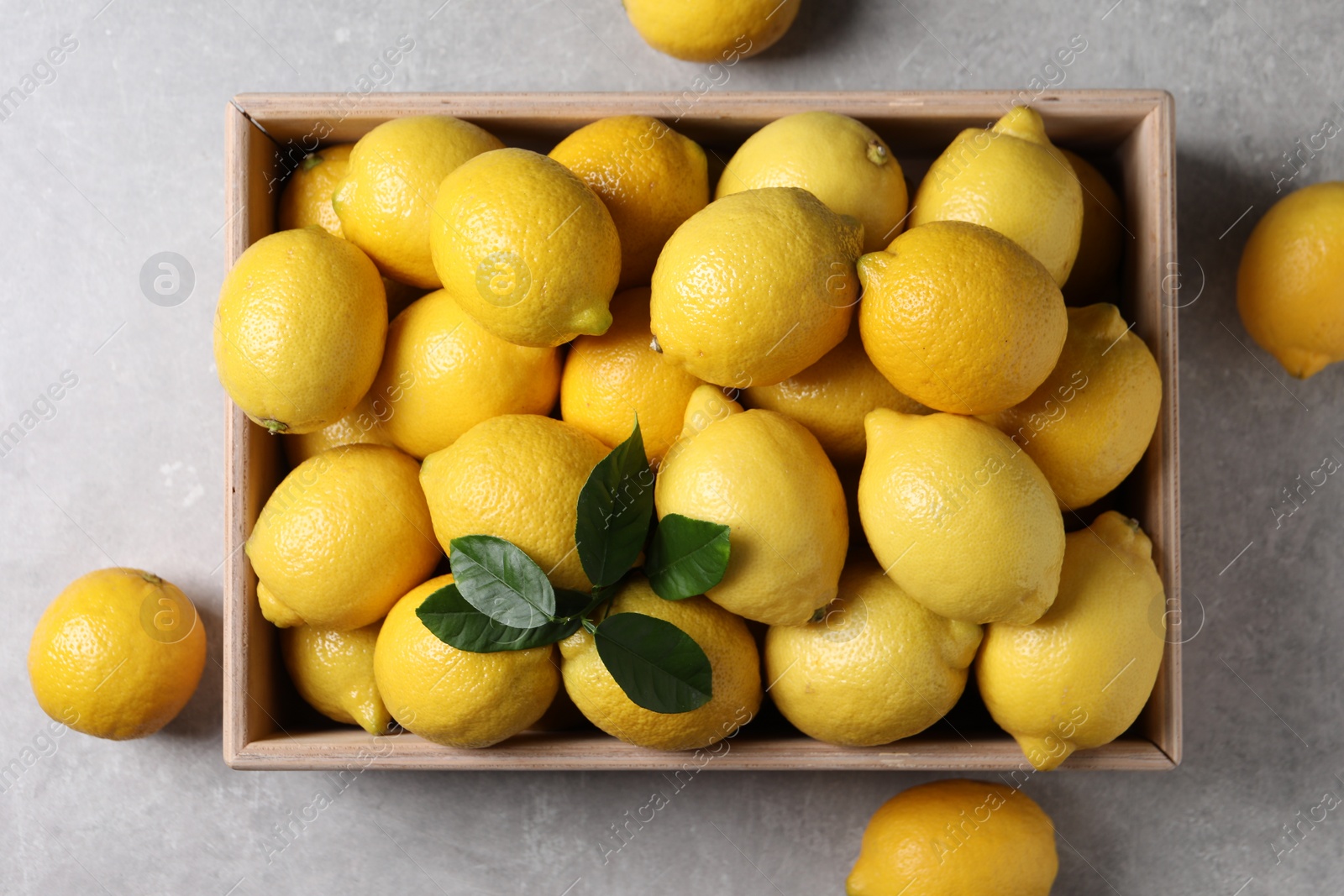 Photo of Fresh lemons in wooden crate on grey table, top view