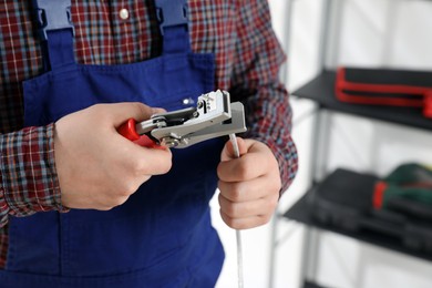 Professional electrician in uniform stripping wiring indoors, closeup