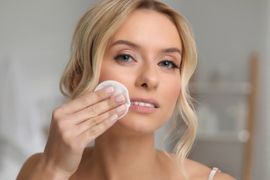 Photo of Beautiful woman removing makeup with cotton pad indoors, closeup