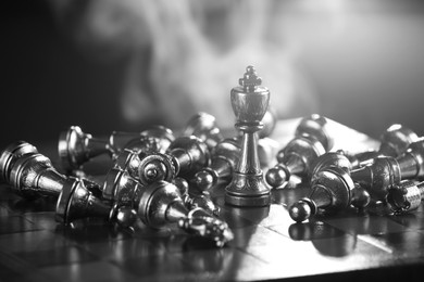 Image of King standing among fallen chess pieces on chessboard, closeup. Black and white effect