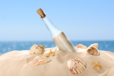 Image of Corked glass bottle with rolled paper note and seashells on sandy beach near ocean