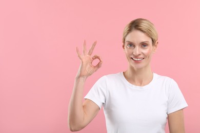 Photo of Woman with clean teeth smiling and showing OK gesture on pink background, space for text