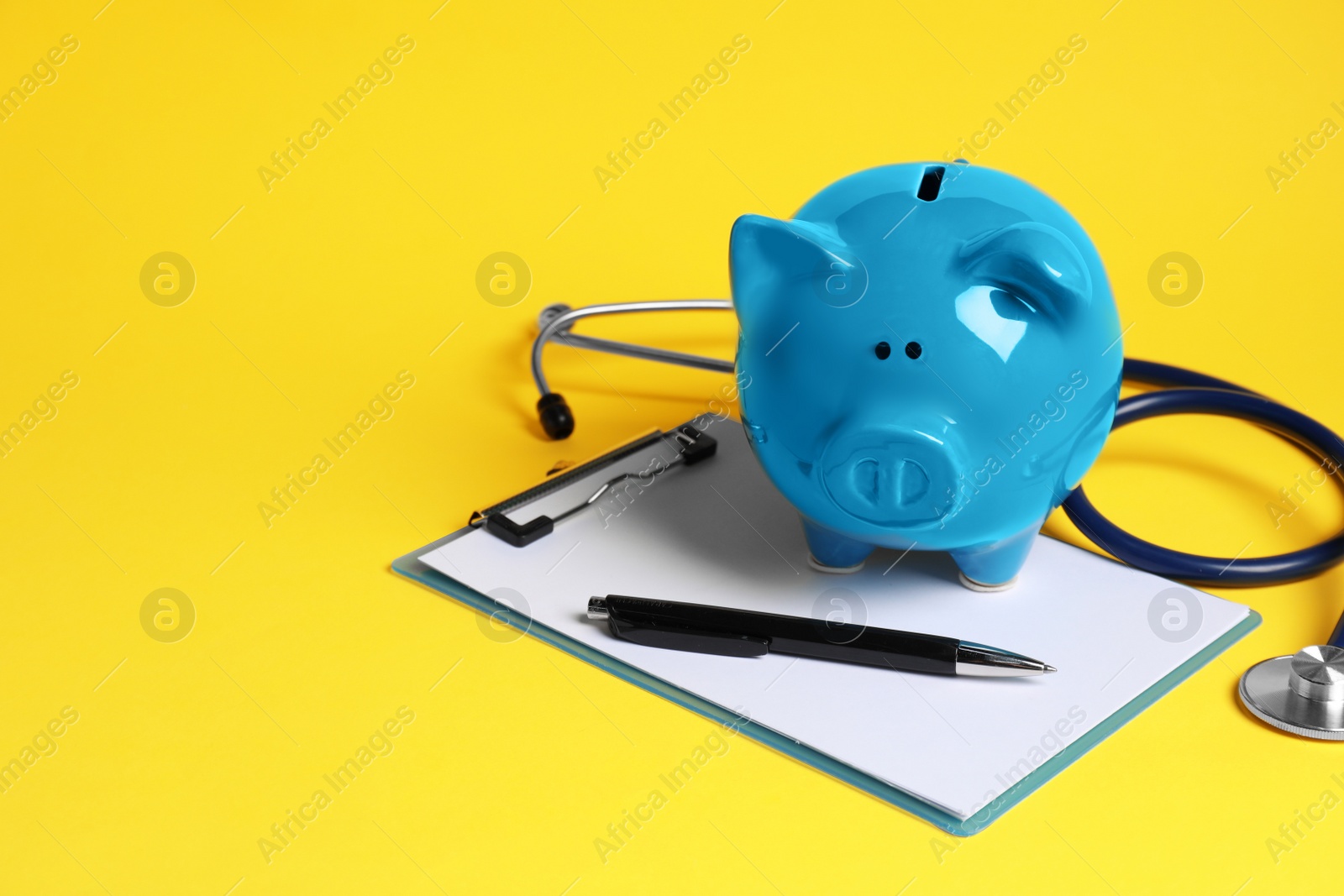 Photo of Piggy bank, stethoscope and clipboard on yellow background, space for text. Medical insurance