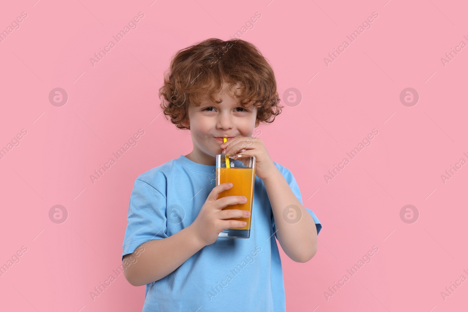 Photo of Cute little boy drinking fresh juice through straw on pink background