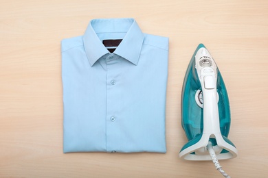 Folded clean clothes and iron on wooden background, top view