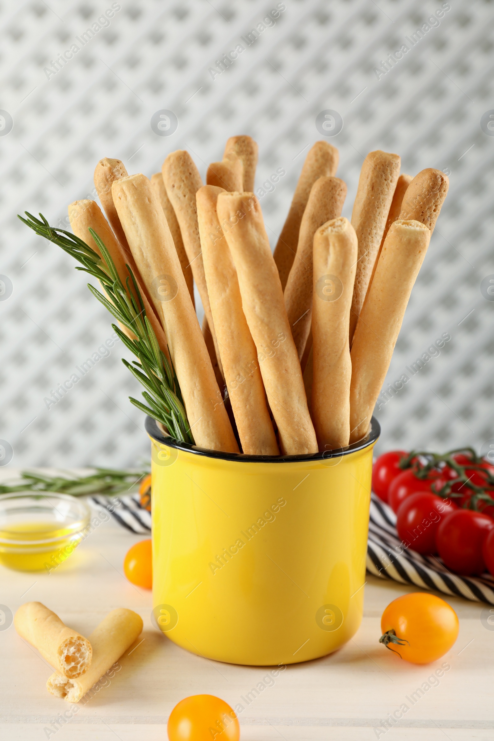 Photo of Delicious grissini sticks, rosemary and tomatoes on white wooden table