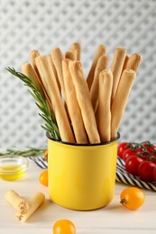 Delicious grissini sticks, rosemary and tomatoes on white wooden table