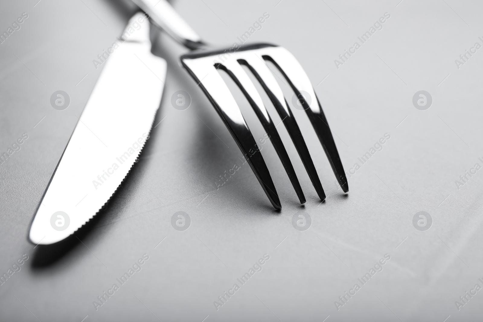 Photo of Shiny fork and knife on grey table, closeup