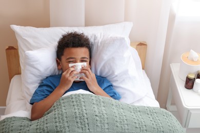 Photo of African-American boy with scarf and tissue blowing nose in bed indoors, above view. Cold symptoms