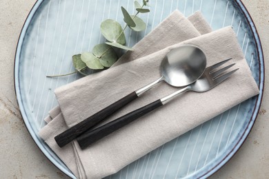 Stylish setting with cutlery, napkin, eucalyptus branch and plate on light grey table, top view