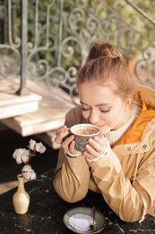 Photo of Young woman enjoying tasty coffee at table outdoors