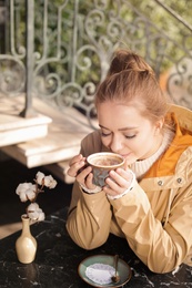 Young woman enjoying tasty coffee at table outdoors