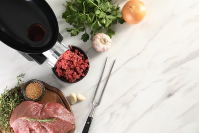 Photo of Electric meat grinder with beef mince and products on white marble table in kitchen, flat lay. Space for text