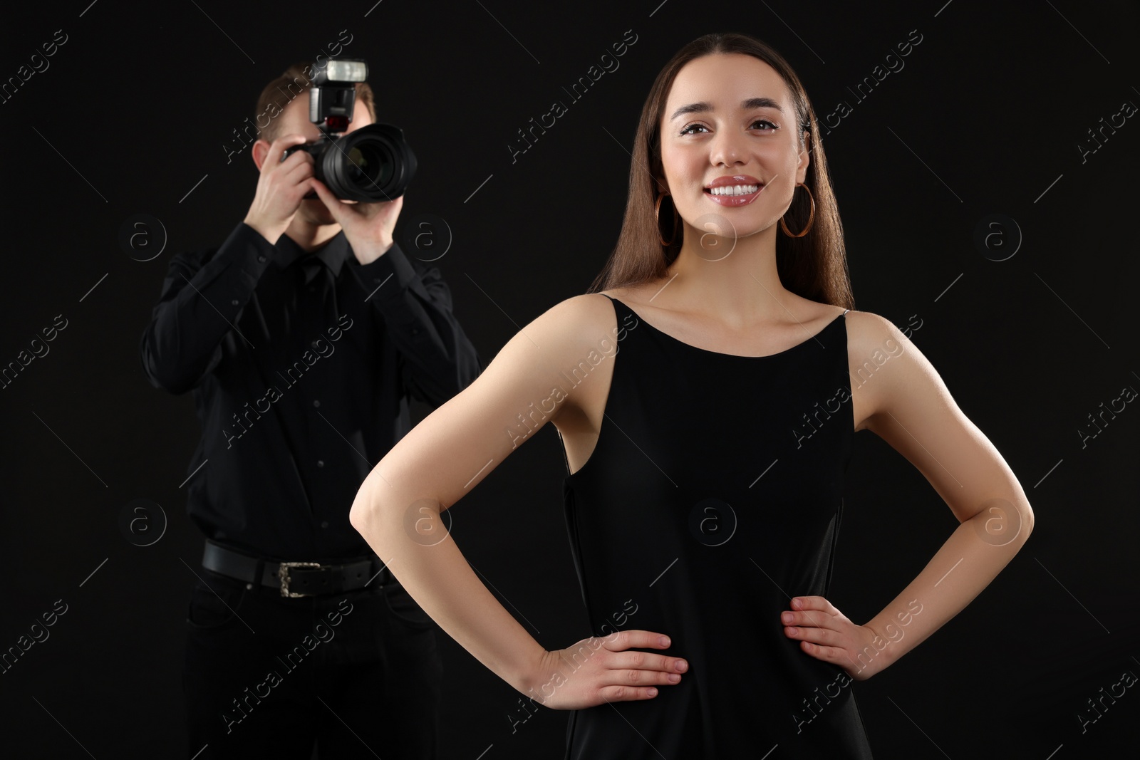 Photo of Professional photographer taking picture of beautiful young woman on black background, selective focus