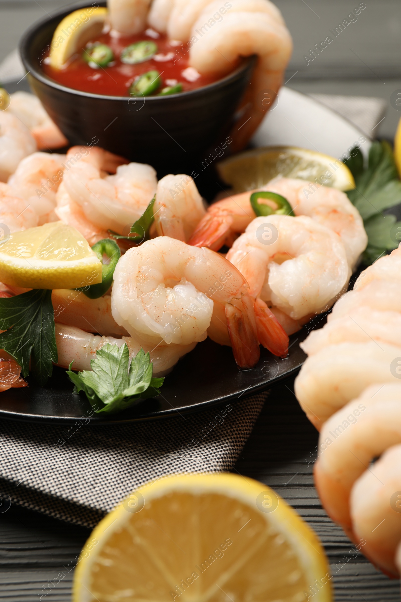 Photo of Tasty boiled shrimps with cocktail sauce, chili, parsley and lemon on table, closeup