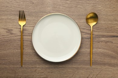 Empty plate, fork and spoon on wooden table, top view