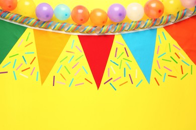 Photo of Bunting with colorful triangular flags and other festive decor on yellow background, flat lay