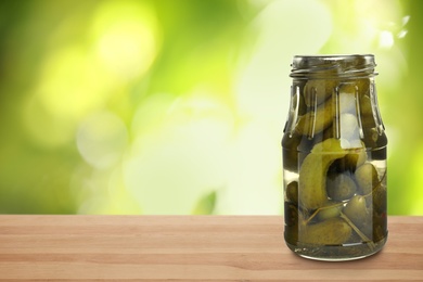 Image of Jar of pickled cucumbers on wooden table against blurred background, space for text 