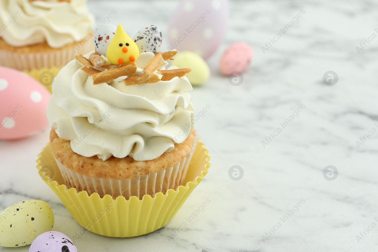 Photo of Tasty Easter cupcake with vanilla cream and candies on white marble table, space for text