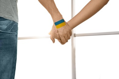 Image of Help for Ukraine. People holding hands with drawing of Ukrainian flag indoors, closeup