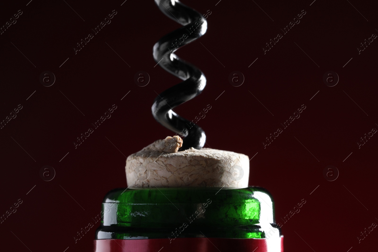 Photo of Opening wine bottle with corkscrew on dark red background, closeup