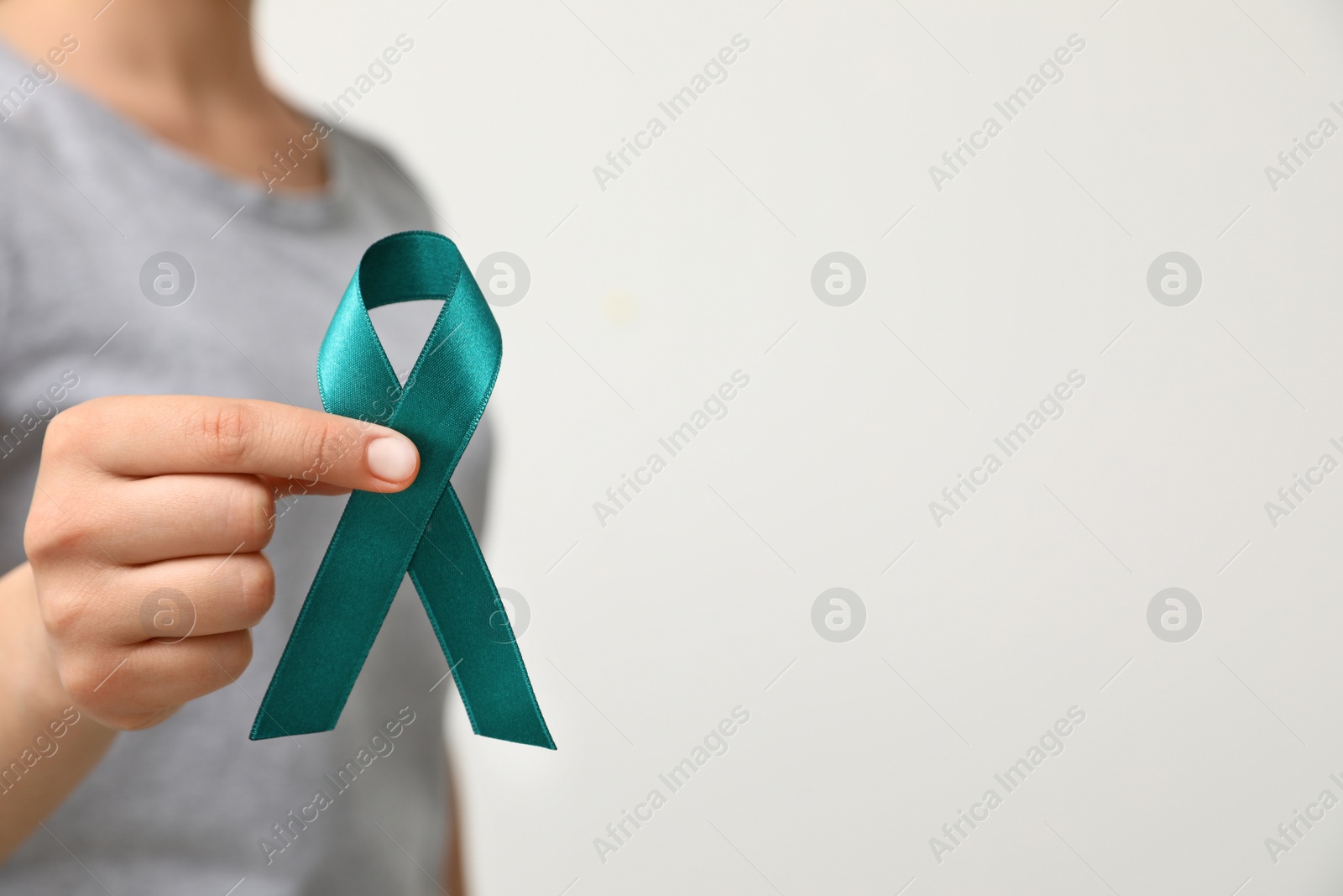 Photo of Woman holding teal awareness ribbon against light background, closeup