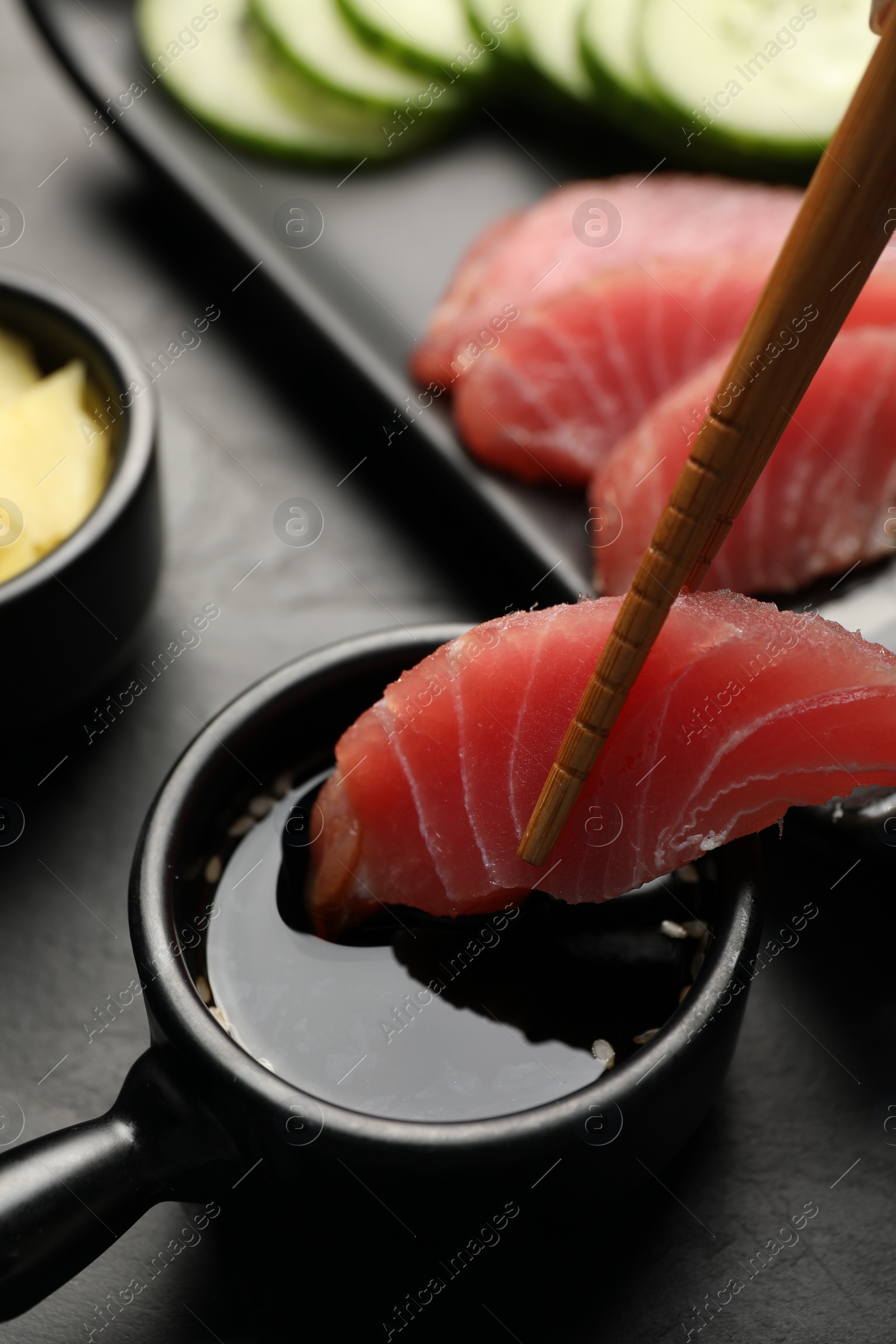 Photo of Dipping tasty sashimi (piece of fresh raw tuna) into soy sauce at black table, closeup