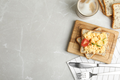 Photo of Tasty scrambled egg sandwich served on light grey marble table, flat lay. Space for text