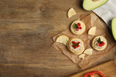 Photo of Delicious crackers with humus, bell pepper and parsley on wooden table, flat lay. Space for text