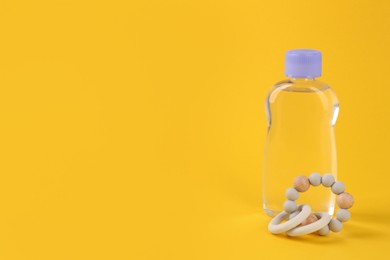 Bottle with baby oil and wooden toy on yellow background. Space for text
