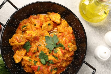 Delicious chicken curry in frying pan and oil on light grey table, top view