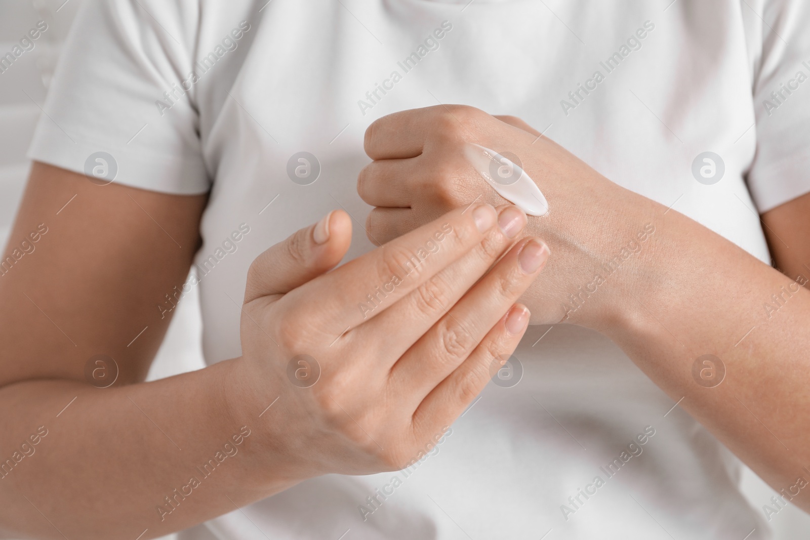 Photo of Woman applying cosmetic cream onto hand on blurred background, closeup