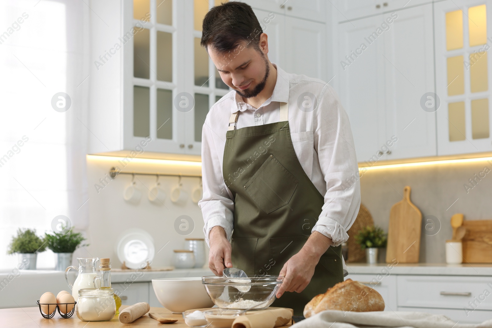 Photo of Making bread. Man putting flour into bowl at wooden table in kitchen