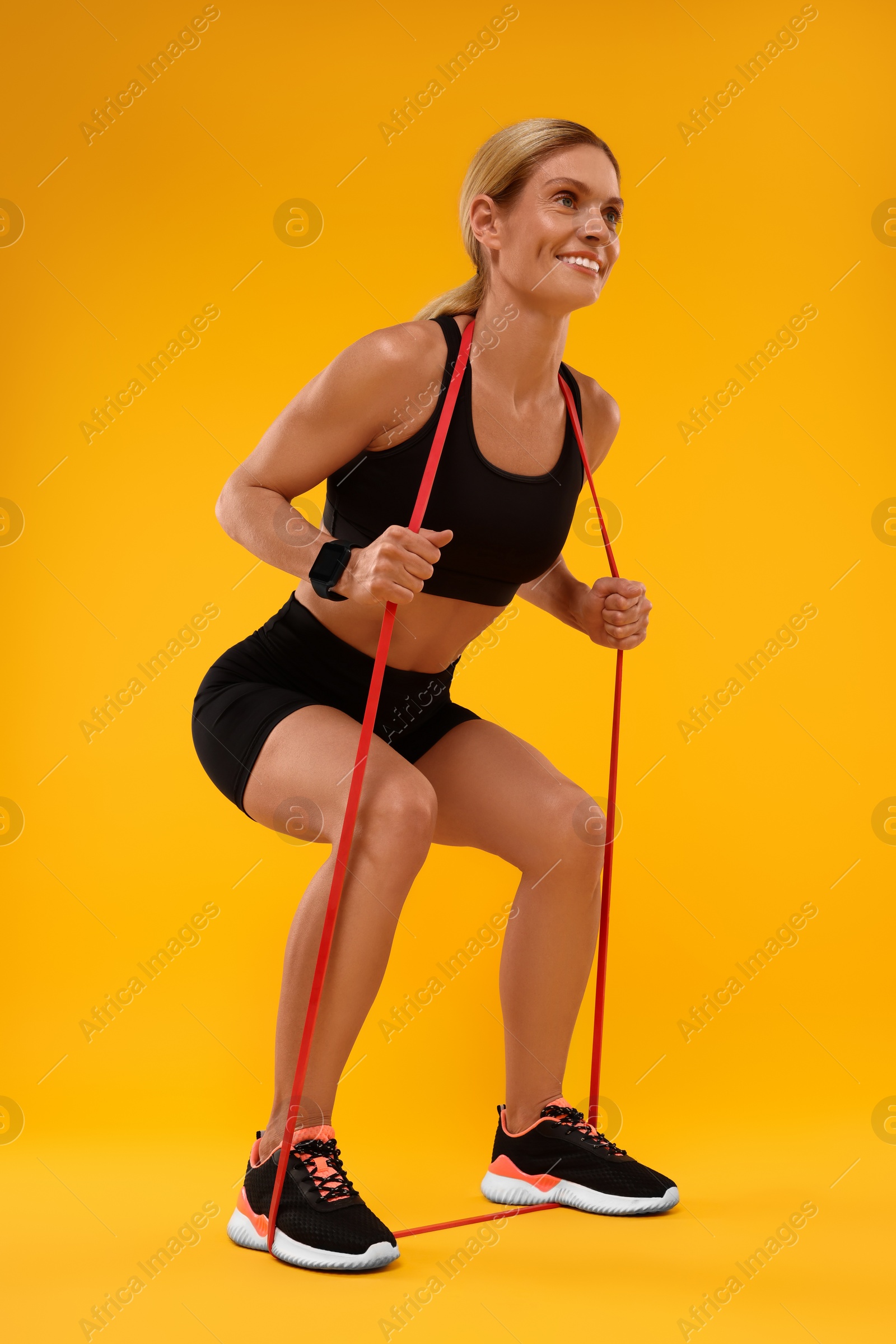 Photo of Woman exercising with elastic resistance band on orange background, low angle view